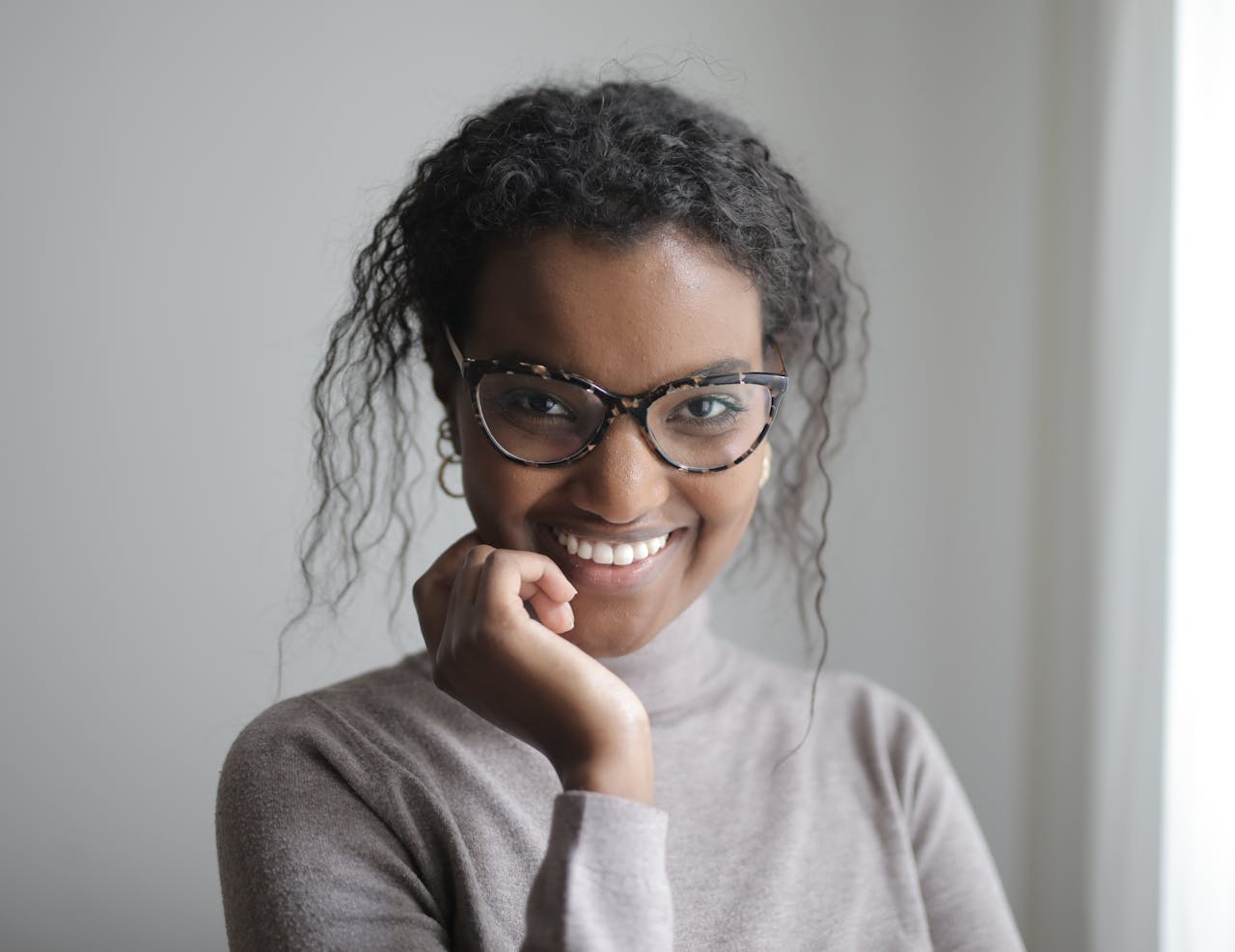 Mastering the First Impression: Your intriguing post title goes here Portrait of a smiling woman with curly hair wearing glasses and a turtleneck indoors.